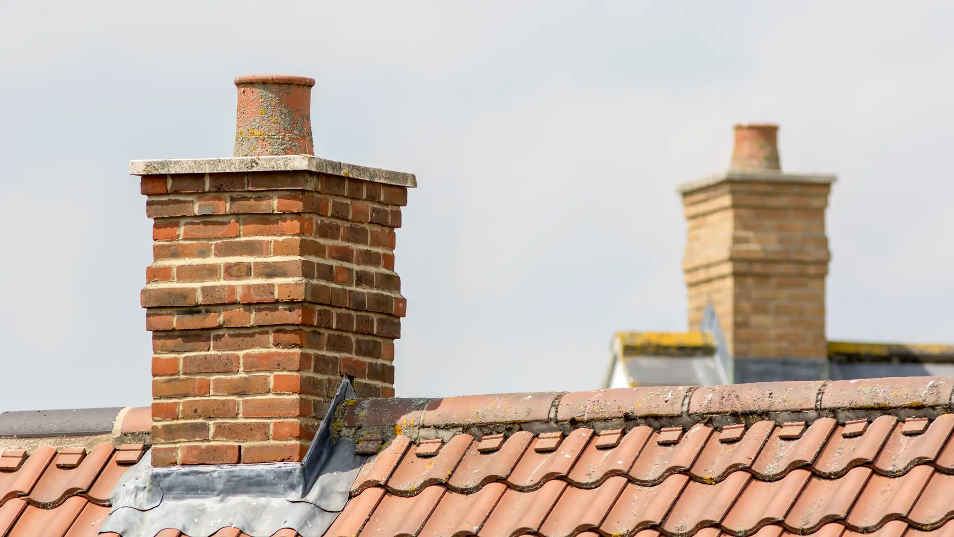 Brick chimney stacks with pots on a red tiled roof