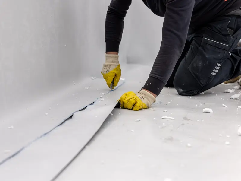 Roofer trimming a flat roof covering at the edge