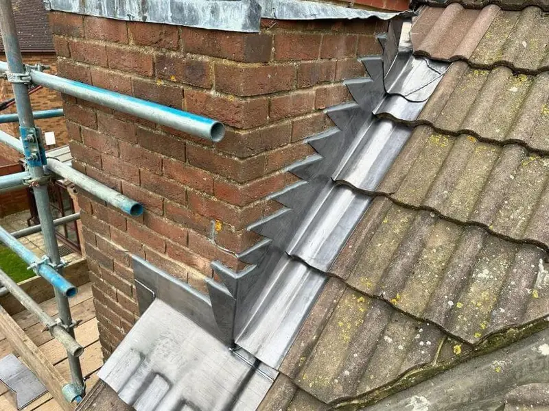 Lead flashing renewed beside a chimney on a tiled roof