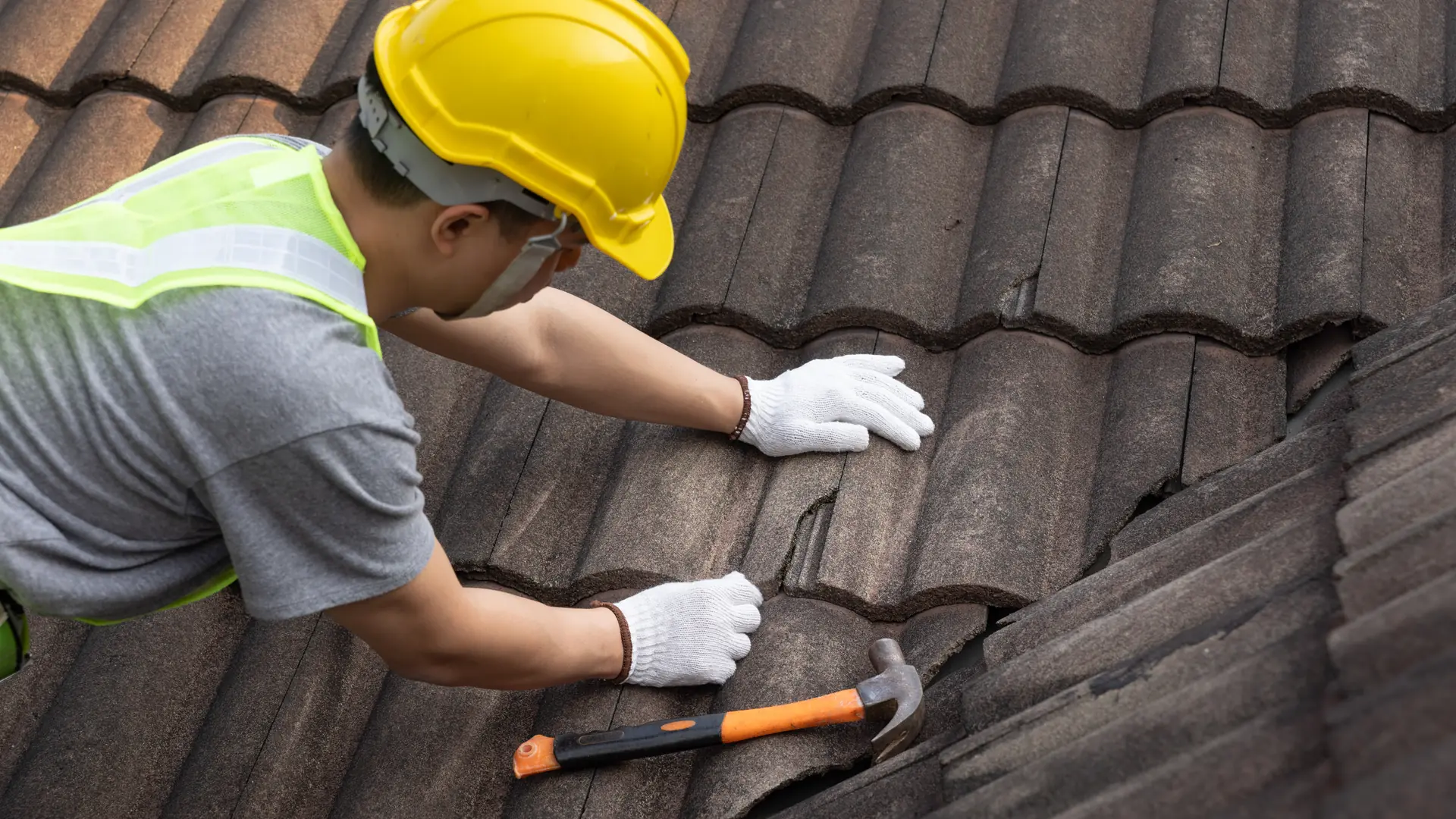 Roofer in a hard hat fixing a concrete roof tile with a hammer