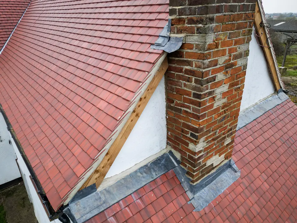 Repaired red tiled roof with new lead flashing at a chimney